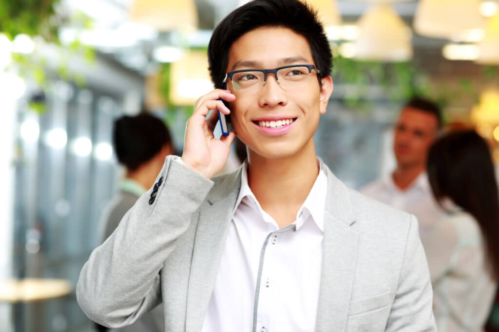 happy businessman talking on the smartphone in front of colleagues